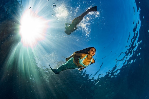 Due sirene che nuotano sott'acqua nel mare blu profondo