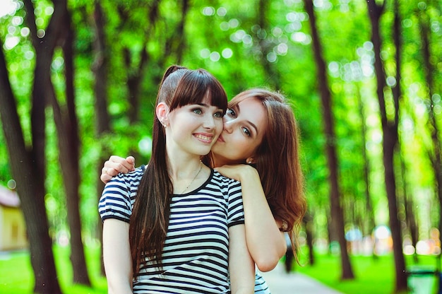 Due sorelle, amiche si divertono, ridono, mangiano zucchero filato, camminano in un parco divertimenti verde d'estate. Felice