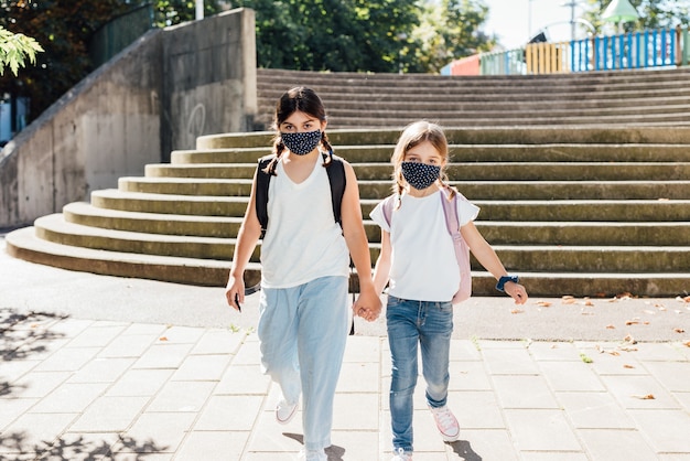 Due sorelle caucasiche di età diverse che vanno a scuola con maschere sul viso a causa della pandemia di coronavirus covid19