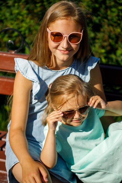 Due sorelle con gli occhiali da sole si siedono nel parco su una panchina d'estate