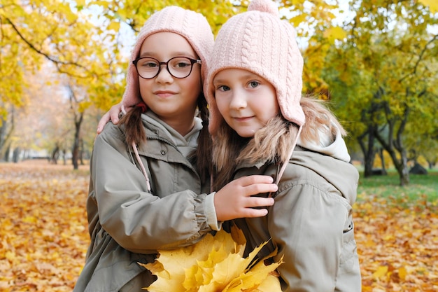 Due sorelle gemelle in posa per la macchina fotografica con un bouquet di foglie gialle nel parco autunnale