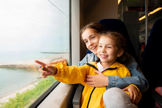 Due sorelle guardano fuori dal finestrino di un treno al mare Vacanze estive in famiglia