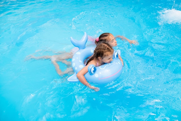 Due sorelle nuotano in una piscina con acqua blu e fanno una vacanza estiva in famiglia con un fan