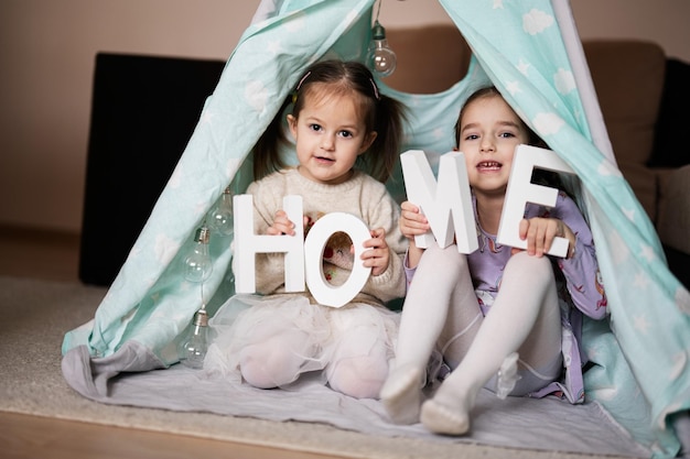 Due sorelle ragazze alla tenda wigwam con lettere domestiche in legno