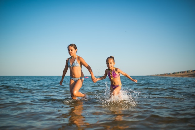 Due sorelle ragazze felici e positive corrono lungo le onde del mare durante le loro vacanze