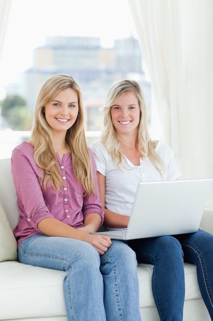 Due sorelle si siedono insieme e sorridono con un computer portatile mentre guardano la telecamera
