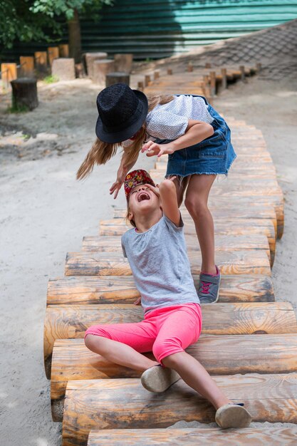 Due sorelle stanno litigando su un sentiero di legno nel parco giochi del parco. Una ragazza ne picchia un'altra. Il bambino sta piangendo.