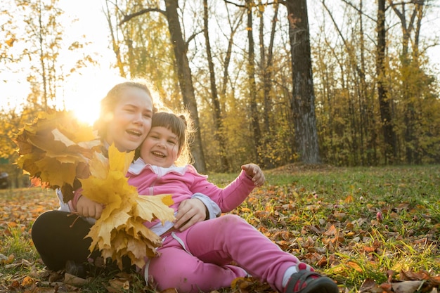 Due sorelle trascorrono del tempo nel parco autunnale e mostrano foglie d'arancio raccolte