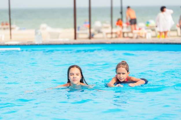 Due sorelline stanno nuotando in una grande piscina con una mia acqua cristallina vicino all'hotel