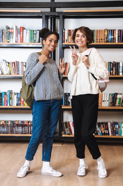 Due studentesse allegre che studiano in biblioteca, portando zaini