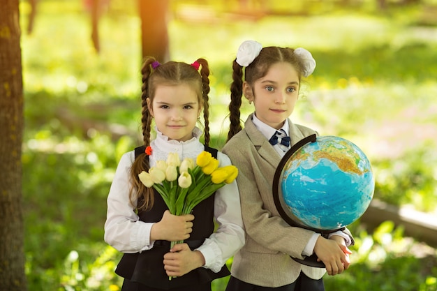 Due studentesse di ragazze caucasiche allegre con fiori e un globo