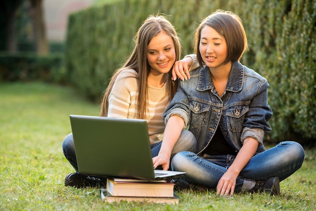 Due studentesse sorridenti stanno sedendo sull'erba.