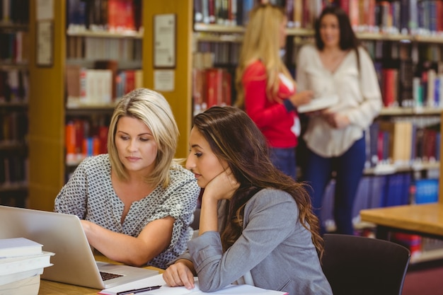 Due studenti concentrati sul portatile con i compagni di classe alle loro spalle