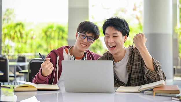 Due studenti maschi asiatici stanno guardando lo schermo del laptop e festeggiano insieme il punteggio del test