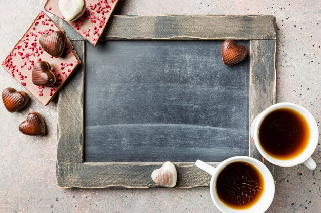 Due tazza di caffè e cioccolatini a forma di cuore su sfondo lavagna per il concetto di San Valentino. Vista dall'alto