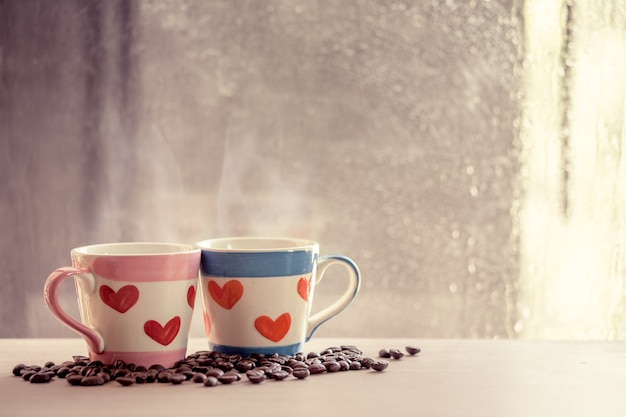 Due tazze adorabili con il chicco di caffè sul fondo della finestra di giorno piovoso. Tonalità di colore vintage