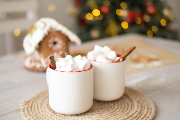 due tazze bianche di cacao con marshmallow e casa di marzapane sul tavolo