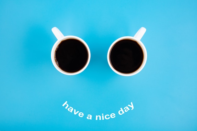 Due tazze da caffè bianche con un sorriso su sfondo blu con la frase Buona giornata