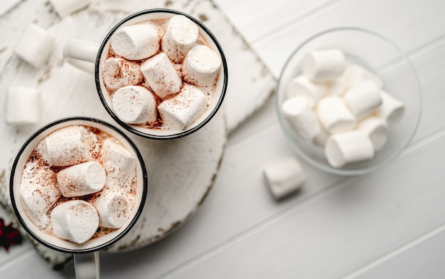 Due tazze di cacao riempite di marshmallow bianco su assi di legno, vista dall'alto