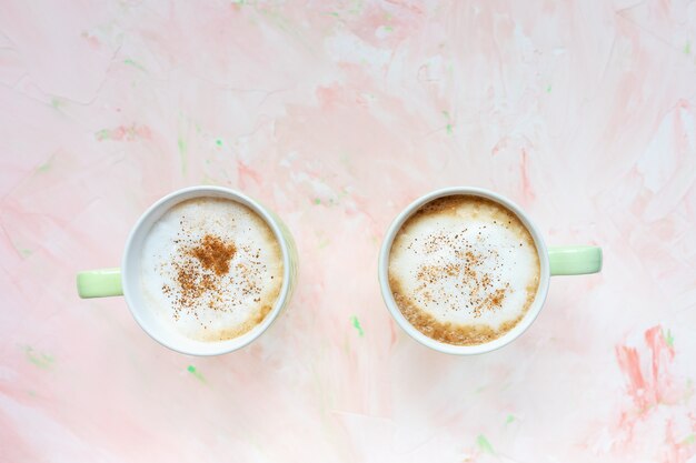 Due tazze di caffè al latte aromatizzato alla cannella sulla parete rustica rosa chiaro. Modello piatto, vista dall'alto, copia spazio, modello di intestazione eroe social media.