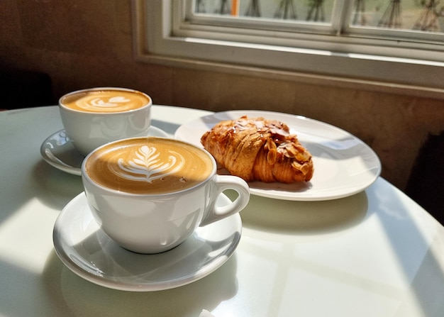 Due tazze di caffè caldo latte art con un croissant