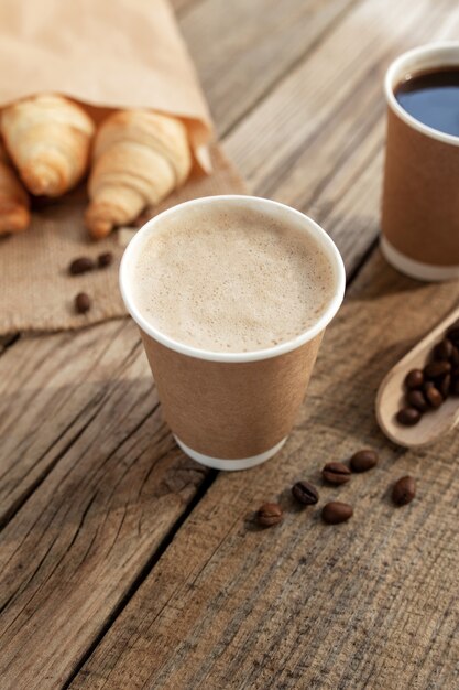 Due tazze di caffè di carta, un pacco di croissant su un sacco, chicchi di caffè tostati essiccati su un cucchiaio su un vecchio tavolo di legno