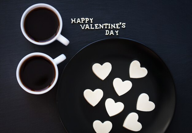 Due tazze di caffè e cioccolatini con bianco a forma di cuore - scritta Happy Valentine