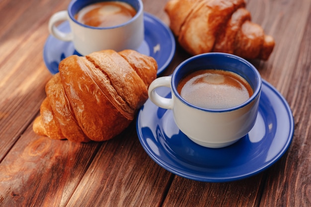 Due tazze di caffè e croissant su uno sfondo di legno, buona luce, atmosfera mattutina