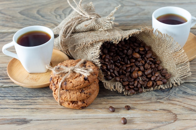 Due tazze di caffè espresso appena fatto su un tavolo di legno. chicchi di caffè e biscotti crunchie su tavolo in legno chiaro, stile rustico, fatto in casa.