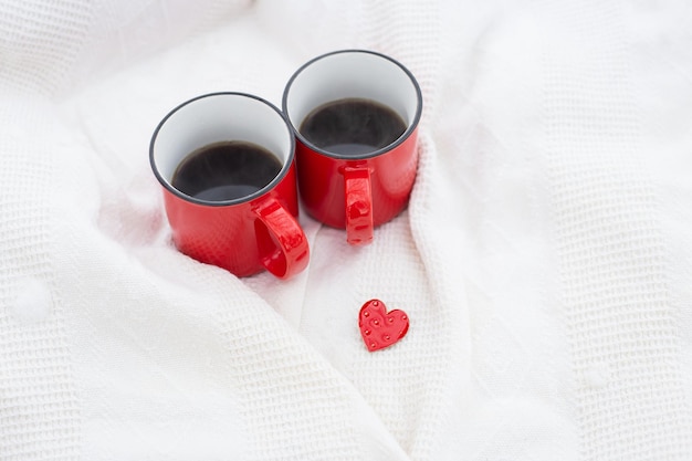 Due tazze di caffè rosse insieme a un cuoricino rosso, caffè a letto. Sorpresa, concetto di celebrazione di San Valentino.