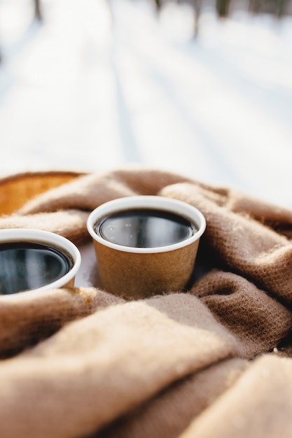 Due tazze di caffè su una sciarpa nel bosco innevato.