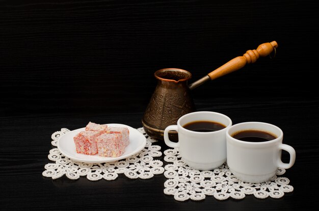 Due tazze di caffè sui tovaglioli di pizzo, pentole e dessert turco su uno sfondo nero