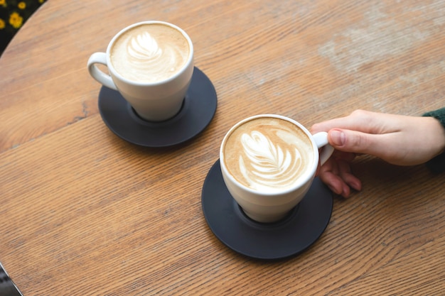 Due tazze di cappuccino su un tavolo di legno con le mani