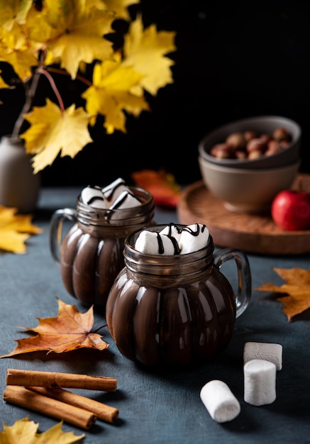Due tazze di cioccolata calda aromatica con marshmallow su uno sfondo scuro con foglie d'acero autunnali Concetto bevanda accogliente Vista frontale e primo piano