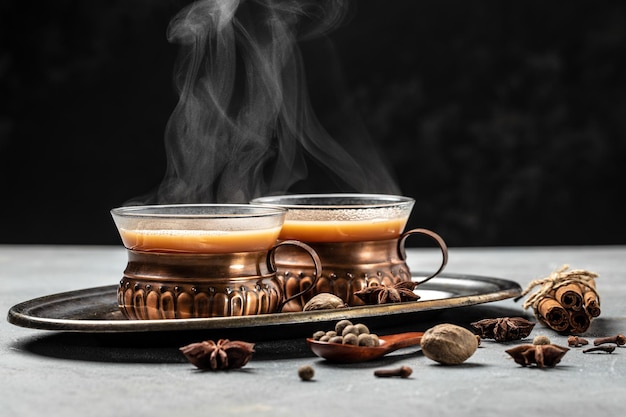 Due tazze di tè masala tè indiano caldo masala chai con latte e spezie in un bicchiere di vetro su sfondo scuro posto per il testo