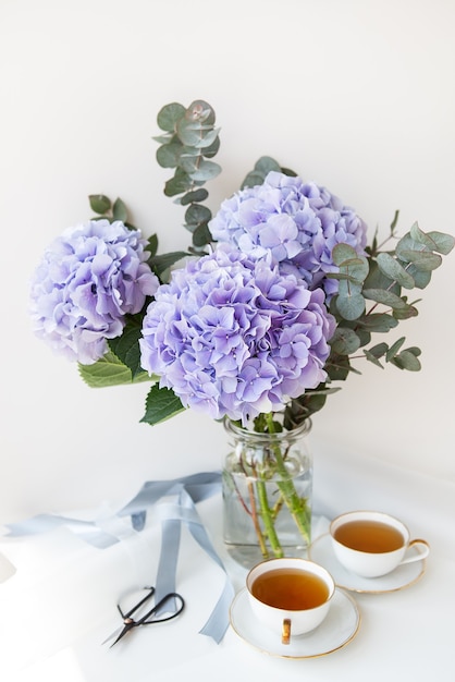 Due tazze di tè nero in una bellissima tazza di porcellana bianca con taglio oro. Bellissimo bouquet di ortensie viola sul tavolo. Concetto di cerimonia del tè.