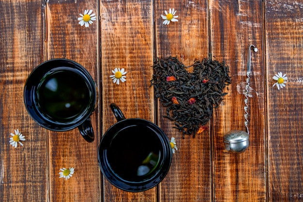 Due tazze di tè vicino a foglie secche di tè nero fanno nel cuore