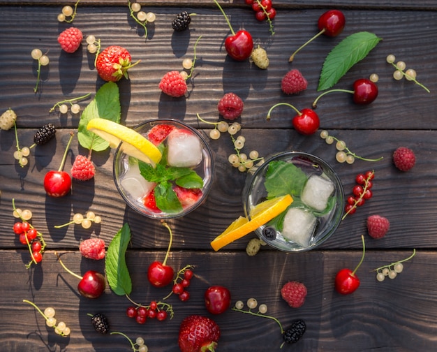 Due tazze di vetro con bevanda alla menta e frutti di bosco sullo sfondo scuro delle tavole