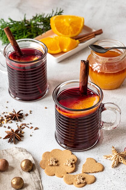 Due tazze di vin brulé caldo con bastoncini di cannella e arancia. Spezie, un vasetto di miele, zenzero cuoco