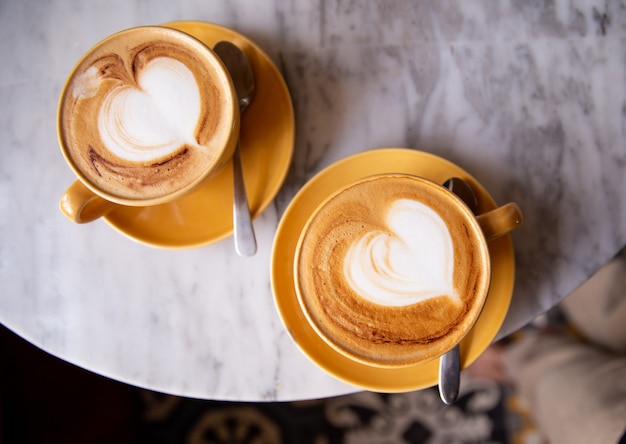 Due tazze gialle di cappuccino caldo sul fondo di marmo della tavola