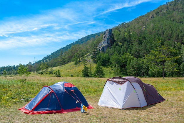 Due tende aperte stanno sull'erba in montagna. Grande roccia e cielo blu sullo sfondo. Campo escursionistico.