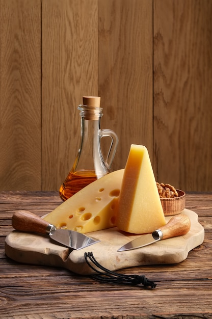Due tipi di formaggi - parmigiano e gouda con noci e miele su tavola di legno con coltelli da formaggio