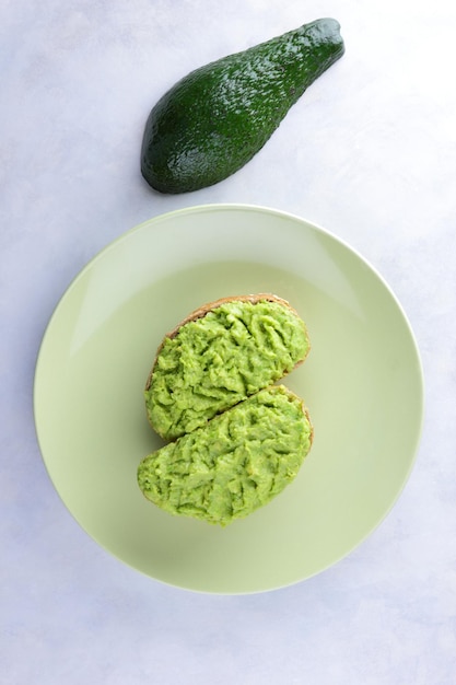 Due toast di avocado verde fresco su un piatto verde Toast e mezzo avocado isolato su sfondo bianco Closeup Vista dall'alto