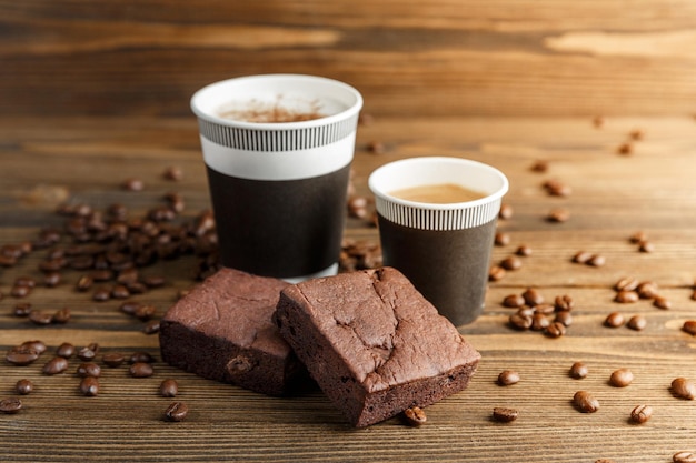 Due torte brownie e tazze di carta di cappuccino e caffè espresso su uno sfondo di legno