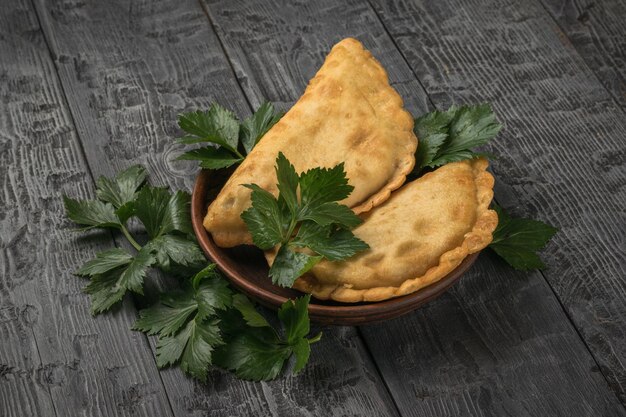 Due torte di carne in una ciotola di argilla e foglie di prezzemolo su uno sfondo di legno