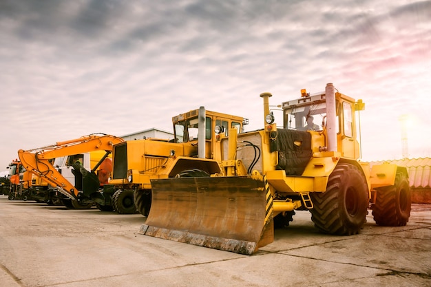 Due trattori a ruote pesanti, un escavatore e altri macchinari per l'edilizia al sole mattutino