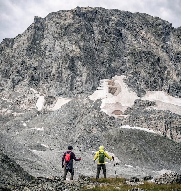 Due uomini attivi con zaino e bastoncini da trekking che camminano sullo sfondo delle montagne rocciose