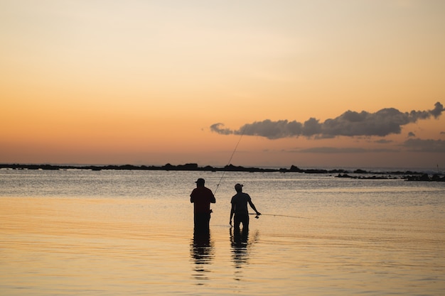 Due uomini che pescano nell'oceano dalla spiaggia al tramonto