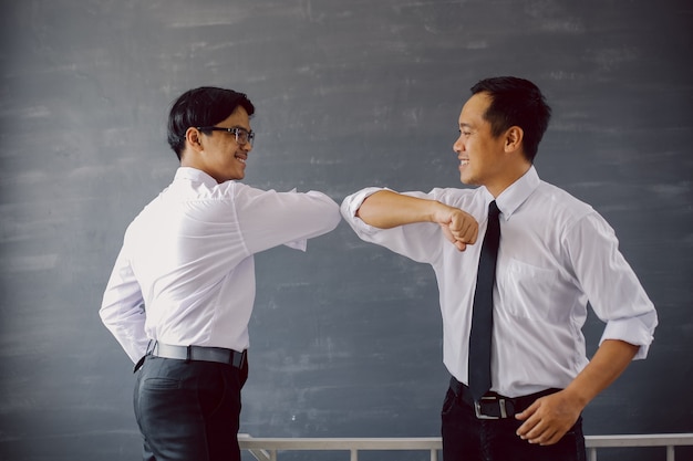 Due uomini d'affari asiatici in camicie bianche che fanno gomitate per evitare il virus corona
