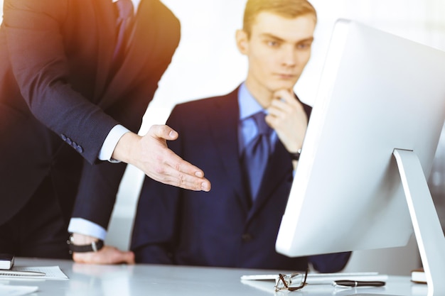 Due uomini d'affari che discutono di domande durante una riunione in un ufficio moderno e soleggiato utilizzando un computer